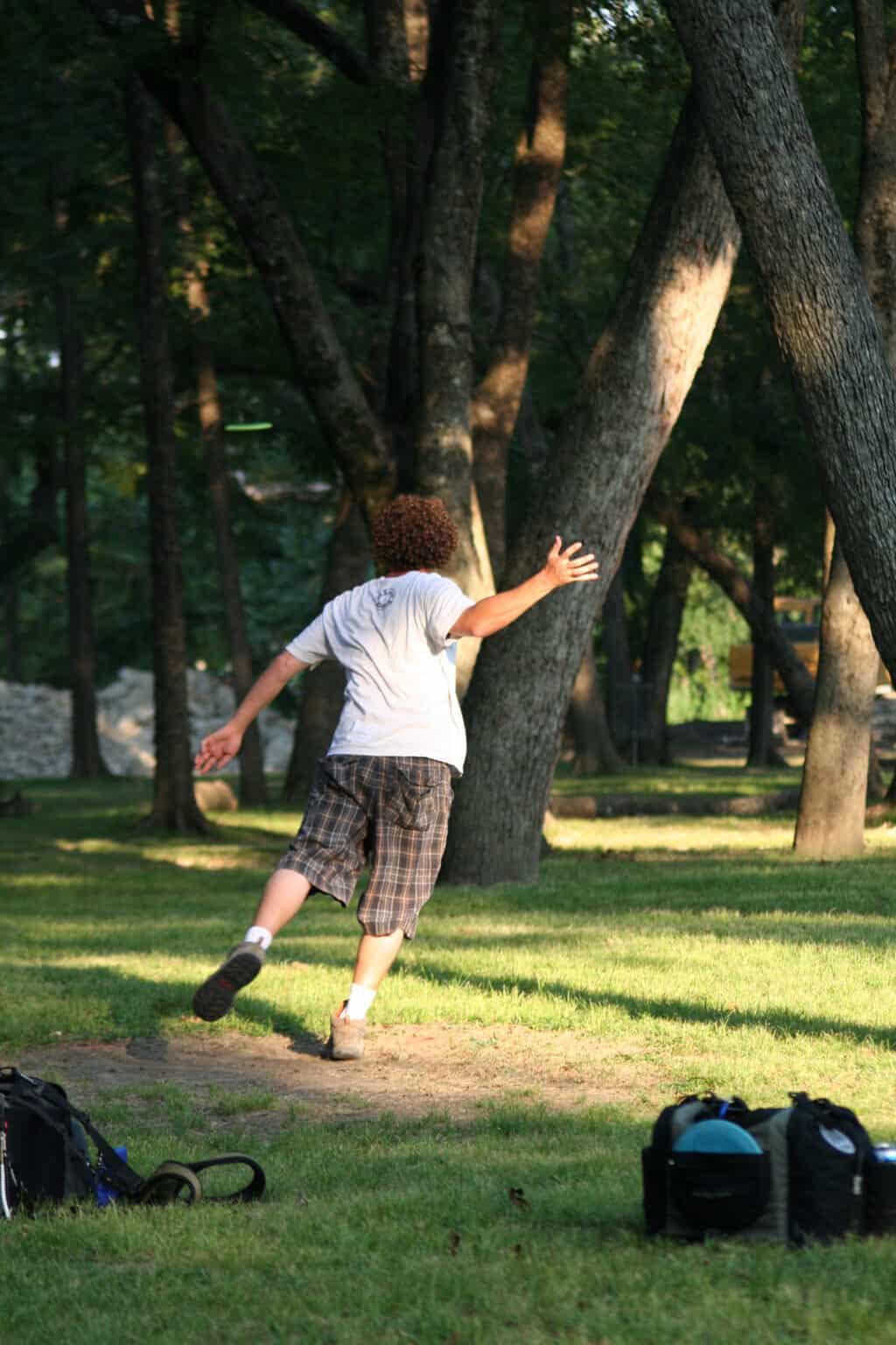Disc golf player reaching for a tree in a park setting.